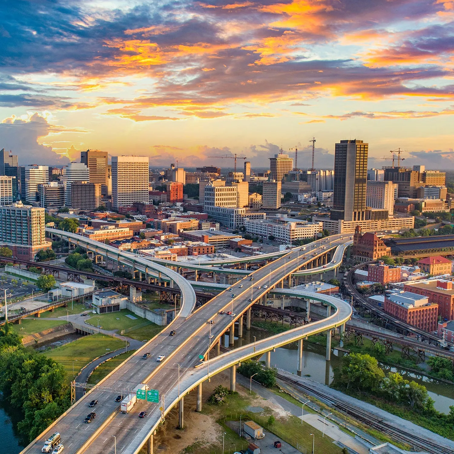 Aerial view of Richmond, Virginia skyline at sunset with highway interchanges in the foreground and dramatic orange and blue sky overhead.